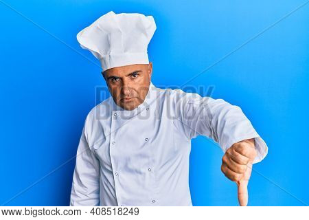 Mature middle east man wearing professional cook uniform and hat looking unhappy and angry showing rejection and negative with thumbs down gesture. bad expression. 