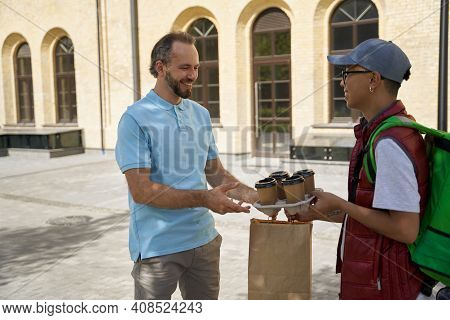 Young Asian Male Courier With Thermo Bag Giving Four Cups Of Cof