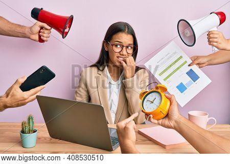 Beautiful hispanic woman working at the office under stress looking stressed and nervous with hands on mouth biting nails. anxiety problem. 