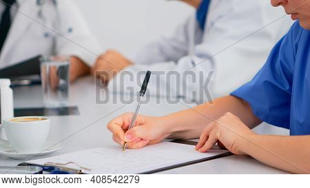 Close Up Of Nurse Writing On Clipboard While Coworkers Discussing In Background Analysing Patients R
