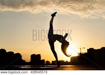 Female Dancer Showing Her Flexibility During Sunset On Cityscape Background With Reflection In The W