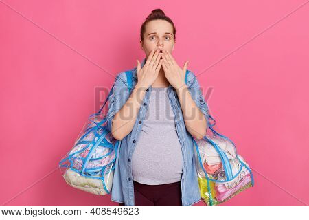 Scared Pregnant Woman Covering Her Mouth With Both Palms, Looks At Camera With Big Eyes, Wearing Cas