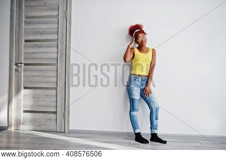 African American Woman In Yellow Singlet And Eyglasses Against White Wall.