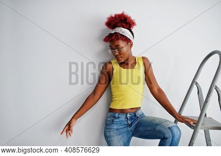 African American Woman In Yellow Singlet And Eyglasses Against White Wall Stand Om Iron Ladder.