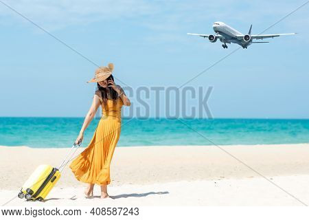 Asia Women Traveler Holding Yellow Luggage Walking And Check In Smart Phone On The Beach. Traveling 