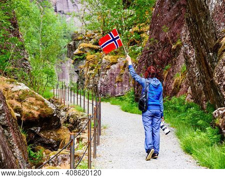 Tourist Woman With Norwegian Flag And Camera Walking Trough Mountains Path In Allmannajuvet Area Sau