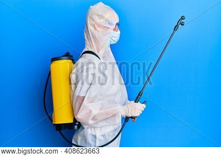 Covid specialist wearing decontamination protective suit and disinfectant spray, decontaminate and sanitize surface, standing over blue background