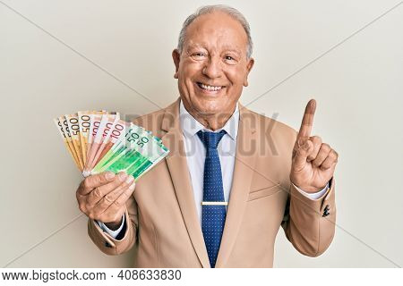 Senior caucasian man holding norwegian krone banknotes smiling with an idea or question pointing finger with happy face, number one 