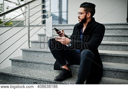Middle Eastern Entrepreneur Wear Black Coat And Blue Shirt, Eyeglasses Against Office Building With