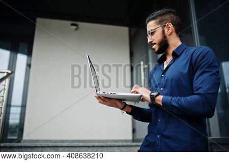 Middle Eastern Entrepreneur Wear Blue Shirt, Eyeglasses With Laptop Against Office Building.