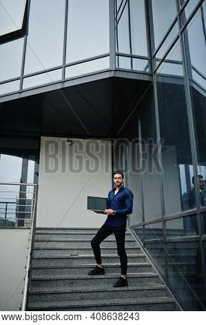 Middle Eastern Entrepreneur Wear Blue Shirt, Eyeglasses With Laptop Against Office Building.