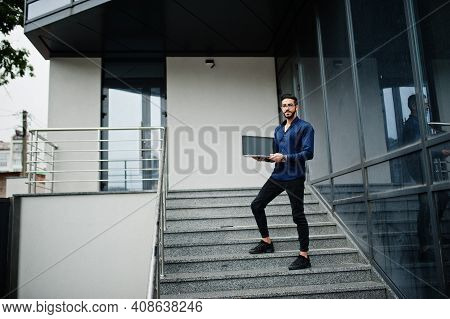 Middle Eastern Entrepreneur Wear Blue Shirt, Eyeglasses With Laptop Against Office Building.