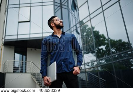 Middle Eastern Entrepreneur Wear Black Coat And Blue Shirt, Eyeglasses Against Office Building.