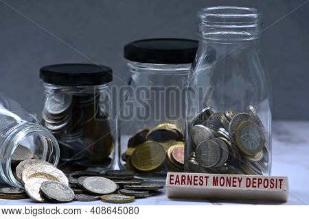 Text On Wood Block And Glass Jars With Multicurrency Coins - Earnest Money Deposit