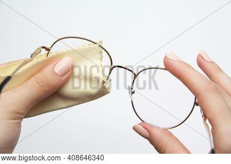 The Girl Manually Cleans The Lenses Of Her Reading Glasses On A Light Background. A Soft Cloth For W