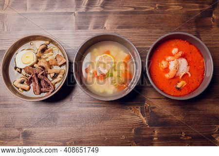 Set Of Serving Asian Soups On Gray Background Top View. Tom Yum Soup, Eel Fish Soup And Ramen Noodle