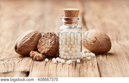 Nutmeg with homeopathic globules nux moschata on wooden background