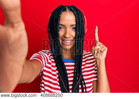 Beautiful hispanic woman taking a selfie photo wearing headphones surprised with an idea or question pointing finger with happy face, number one 