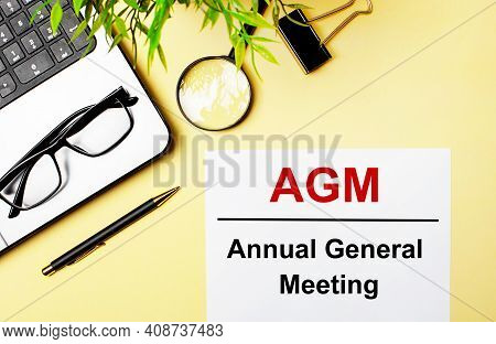 Agm Annual General Meeting Is Written In Red On A White Piece Of Paper On A Light Yellow Background 