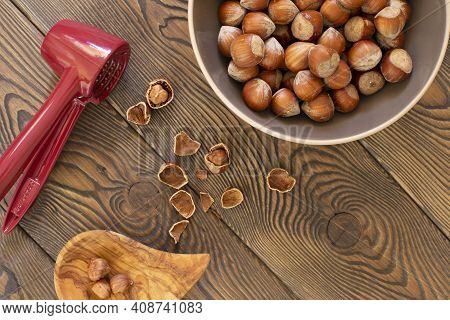 Hazelnuts With A Red Nutcracker In A Bowl On A Wooden Board, Nutshell, Dark Photo, Flat Lay