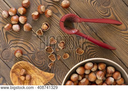 Hazelnuts With A Red Nutcracker In A Bowl On A Wooden Board, Nutshell, Dark Photo, Flat Lay