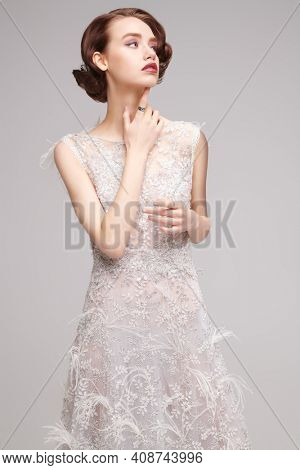 Portrait of a charming young woman in a luxury white dress on a gray background. Evening makeup and hairstyle of the 20s. 
