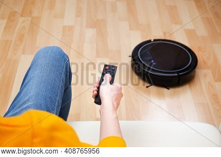Man Resting While Robotic Vacuum Cleaner Doing Chores, Clean Work At Home. Man Controls A Robot Vacu