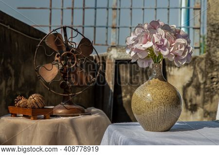 Bouquet Of Purple Flowers In Handmade Ceramic Vase On White Textured Table Cloth And Vintage Fan Wit