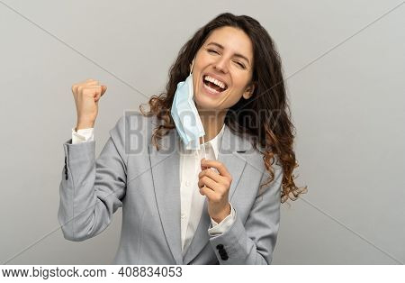 Studio Portrait Of Happy Business Woman Taking Off Mask, Raising Fist, Grey Background. Female Remov