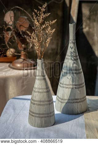 Dried Flowers In Two Ceramic Vase On White Textured Table Cloth And Vintage Fan With Old Cement Wall