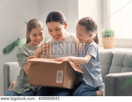 Mother and daughters are unpacking cardboard box at home.