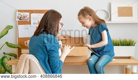 Mother and daughter are unpacking cardboard box at home.