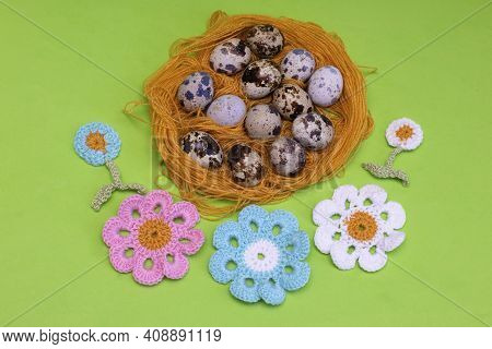 Quail Eggs In An Impromptu Nest Of Threads On A Green Background And Knitted Flowers. Decoration For