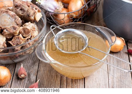 Passing The Bone Broth Through A Sieve. Concentrated Bone Broth In A Bowl