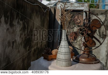 Dried Flowers In Ceramic Vase On Pink Textured Table Cloth And Vintage Fan With Old Cement Wall. Hom