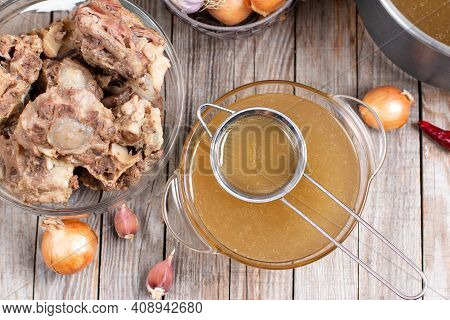 Passing The Bone Broth Through A Sieve. Concentrated Bone Broth In A Bowl
