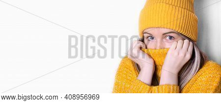 Young Woman Wearing Yellow Beanie Is Pulling Her High Neck Sweater Up To Keep Warm. Wide Banner With
