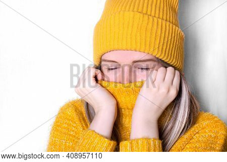 Young Woman Wearing Yellow Beanie Is Pulling Her Sweater Collar Up To Keep Warm