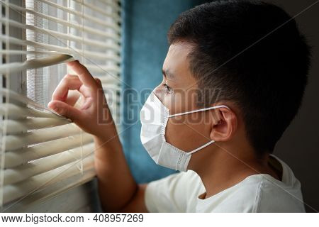 Asian Boys Wearing A Face Mask, And Looking Out The Window With Loneliness And Sadness. Coronavirus 