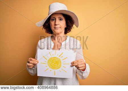 Middle age curly woman on vacation holding bunner with sun image over yellow background with a confident expression on smart face thinking serious