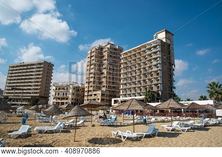 Famagusta, Cyprus - September 15 2016: Palm Beach With Beach Umbrellas And Tourists And The Abandone
