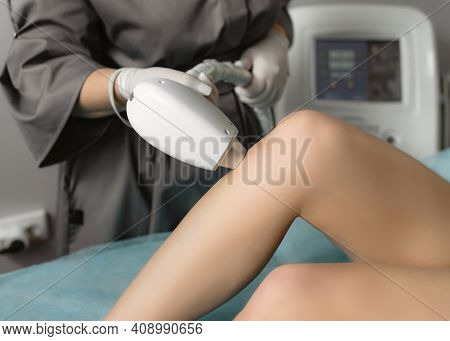 Beautician Removing Hair On Female Legs Using A Laser. Close-up Photo Of Cosmetologist Hand With Las