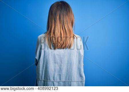 Middle age beautiful woman wearing casual shirt standing over isolated blue background standing backwards looking away with crossed arms