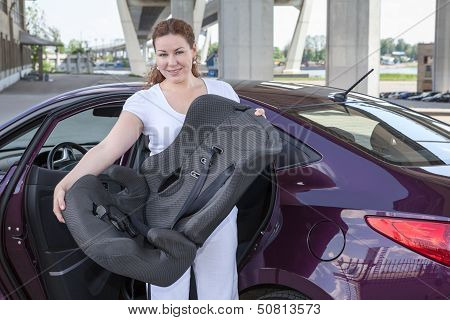 Mother Holding Infant Restraint Chair Near Own Car
