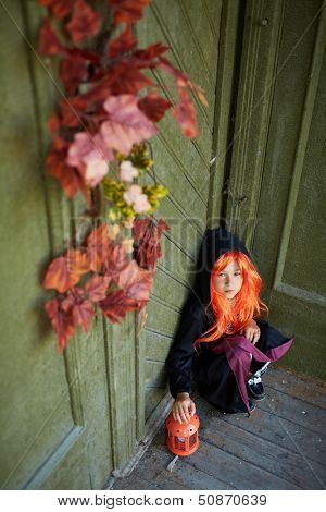 Portrait of Halloween girl with red hair sitting on the porch of dilapidated house