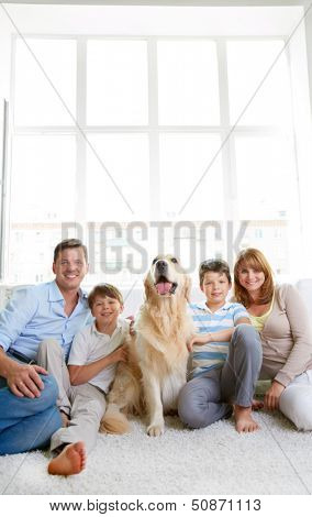 Cheerful family with their pet sitting on the floor at home