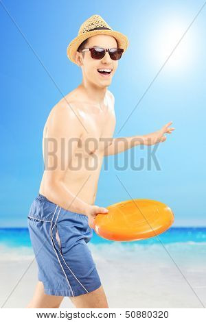 Smiling guy in swimming shorts throwing frizbee, on a beach enjoying the sun