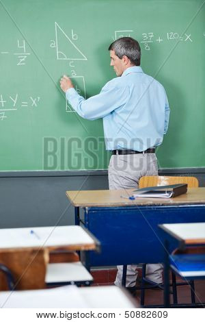 Rear view of male professor solving mathematics on greenboard in classroom