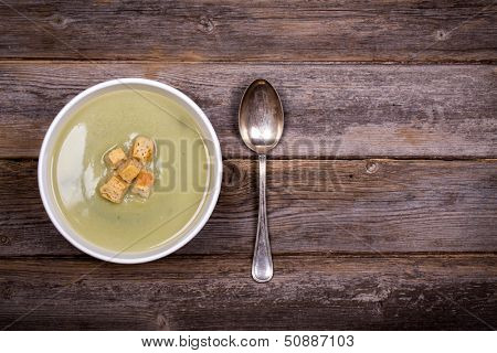 A bowl of leek and potato soup with bread croutons, over old wood table with fresh leeks and potatoes alongside