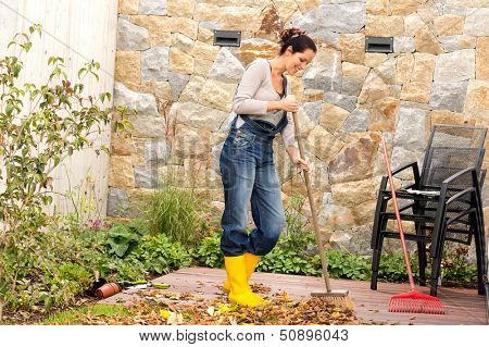 Young woman sweeping autumn leaves veranda backyard cleaning pile